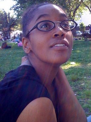 A woman with glasses sitting in the grass.