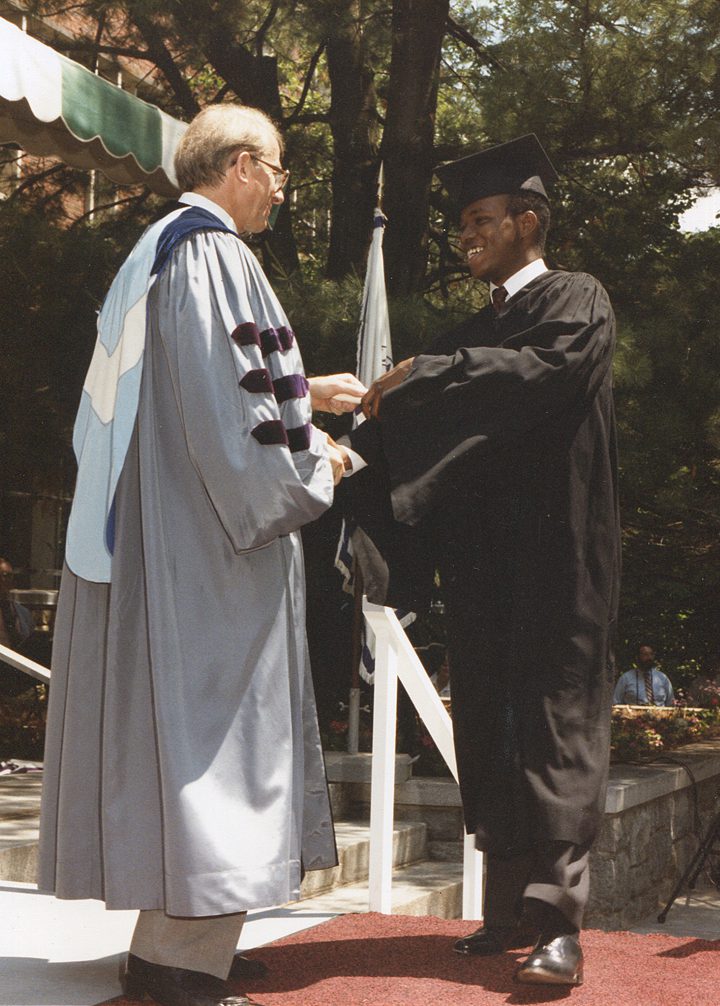 A man in graduation attire is shaking hands with another person.
