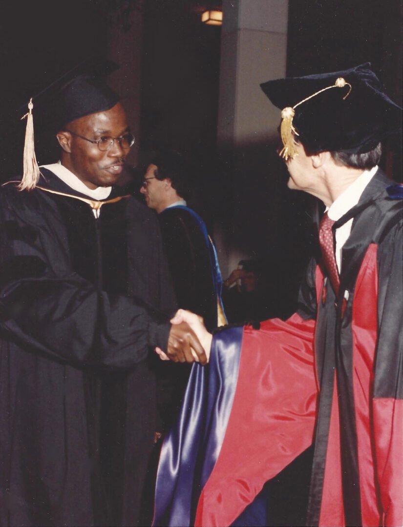A man in graduation cap and gown shaking hands with another person.