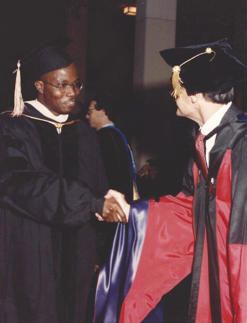 A man in graduation cap and gown shaking hands with another person.