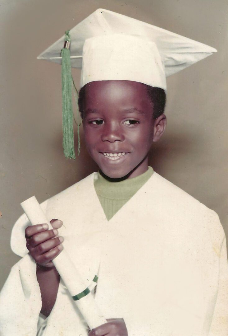 A young boy in graduation attire holding his diploma.