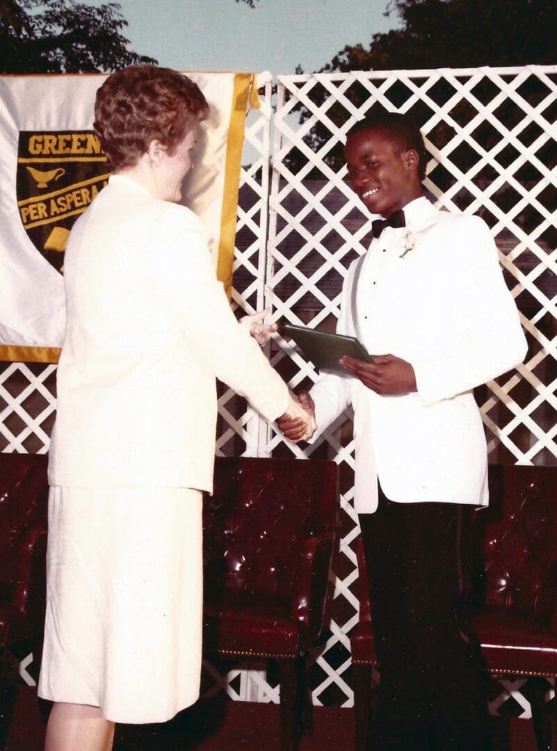 A man and woman are shaking hands in front of a fence.