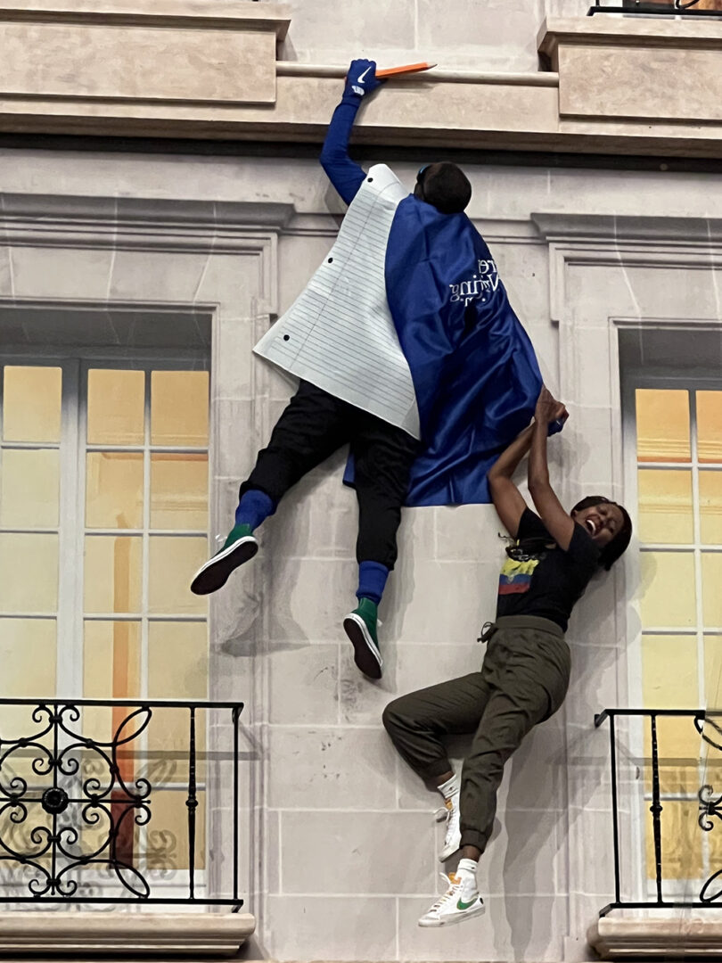 Two men are hanging from a building with one of them falling.