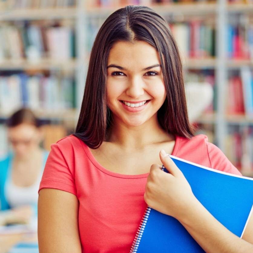 A girl holding a blue book in front of some books