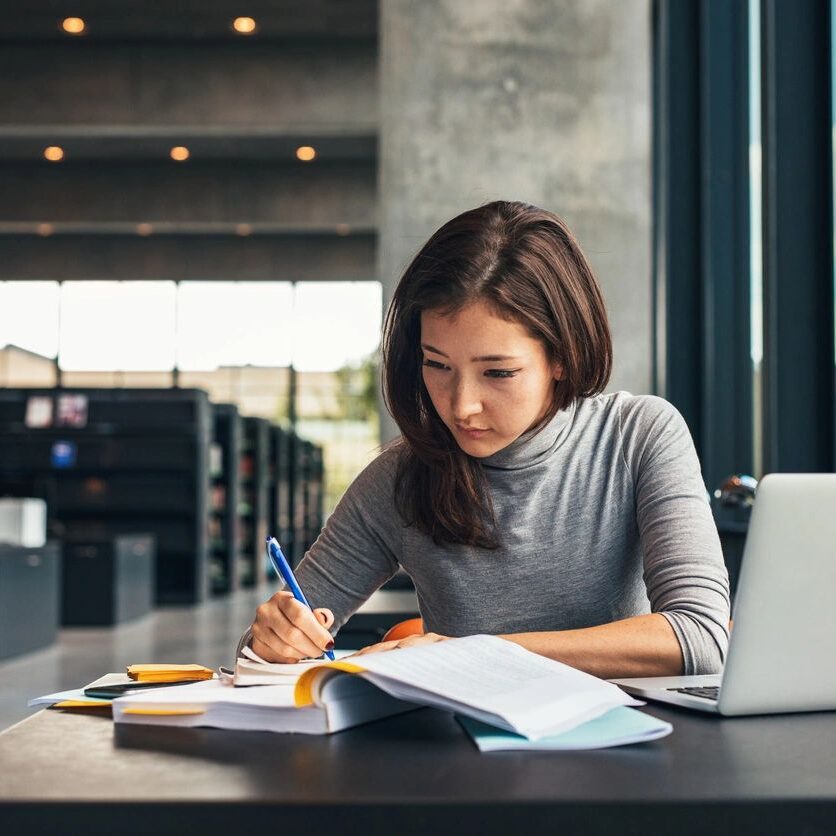 A woman sitting at a table writing on paper.